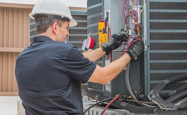 Technician testing electrical connections on outdoor HVAC equipment